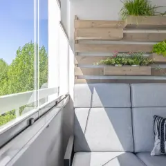 Przytulny balkon wnękowy z szarą sofą, zielenią i widokiem na drzewa.