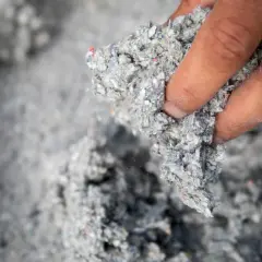 Dłoń trzyma kłębek szarej, włóknistej masy. To celuloza, materiał izolacyjny z recyklingu.
