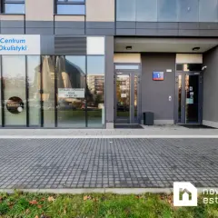 Elewacja budynku z witrynami sklepów: Centrum Okulistyki, Żabka. Widoczne szyldy i wejścia.