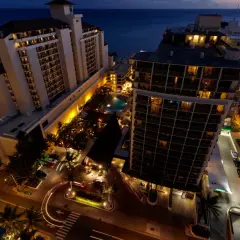Wieczorem widać kompleks condo hotel z basenem i palmami. Światła budynków i ulic tworzą ciepłą atmosferę.