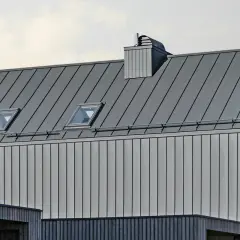 Nowoczesny dach z blachy na rąbek, z oknami dachowymi i kominem. Sprawdź blacha na rąbek cena za m2.