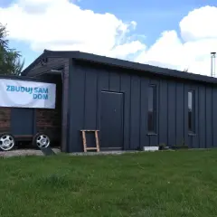 Mobilny garaż bez pozwolenia 70m2, z drewnianą częścią na przyczepie i ciemnoszarą, nowoczesną bryłą.