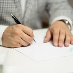 Mężczyzna w eleganckim garniturze podpisuje dokument, finalizując cesję umowy deweloperskiej.