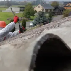 Pracownik w kombinezonie usuwa eternit z dachu. Azbest w eternicie stanowi zagrożenie.