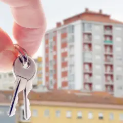 Klucze do mieszkania w tle bloku. Zastanawiasz się, jak sprawdzić czy mieszkanie jest zadłużone?