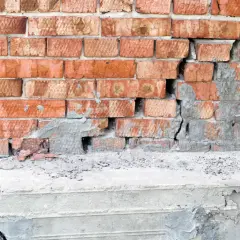 Uszkodzony mur z cegły i pęknięty betonowy cokół. Rozważasz podbijanie fundamentów? Cena może być wysoka.