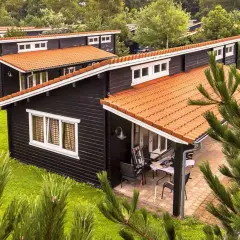 Czarny bungalow z pomarańczowym dachem, otoczony zielenią. Idealne miejsce na wakacje, zastanawiasz się bungalow co to?