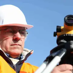 Geodeta w kasku i kamizelce odblaskowej pracuje z niwelatorem. Zastanawiasz się, ile kosztuje geodeta?