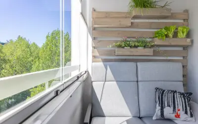 Przytulny balkon wnękowy z szarą sofą, zielenią i widokiem na drzewa.