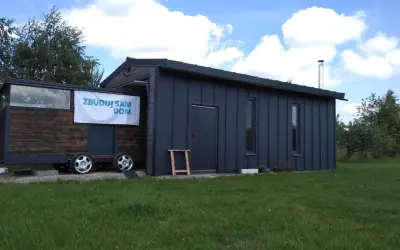 Mobilny garaż bez pozwolenia 70m2, z drewnianą częścią na przyczepie i ciemnoszarą, nowoczesną bryłą.
