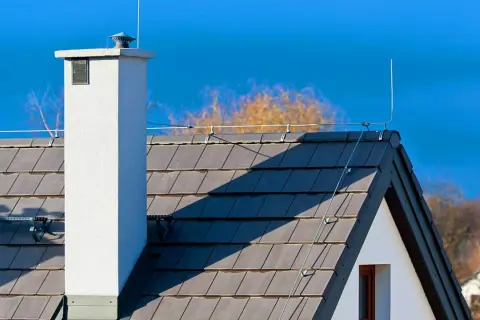 Dach z dachówką i kominem, na którym widoczna jest instalacja odgromowa. Cena takiej ochrony domu jest inwestycją w bezpieczeństwo.
