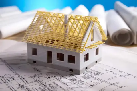 Model domu na planach architektonicznych, z widoczną konstrukcją dachu. Zastanawiasz się, ile kosztuje adaptacja projektu?