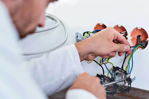 Elektryk podłącza przewody. Zastanawiasz się, ile kosztuje wymiana instalacji elektrycznej? Sprawdź!