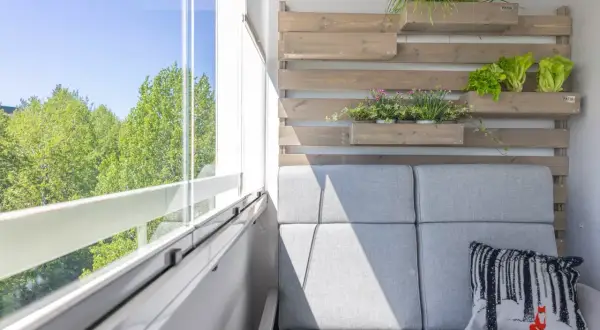 Przytulny balkon wnękowy z szarą sofą, zielenią i widokiem na drzewa.