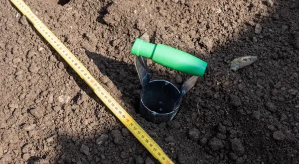 Przyrząd do pobierania próbek gleby i miarka leżą na ziemi. To część badania geotechnicznego gruntu, które pomoże określić jego cenę.