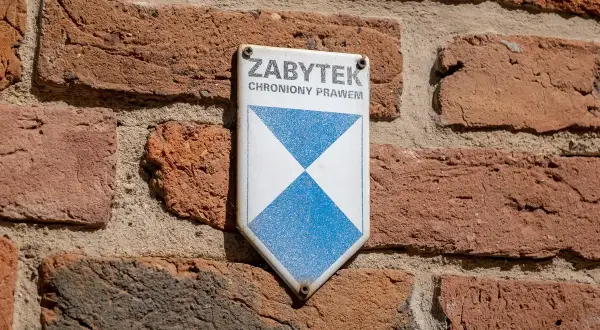 Tabliczka "ZABYTEK CHRONIONY PRAWEM" na ceglanej ścianie. To znak, że obiekt wymaga troski i konserwacji.