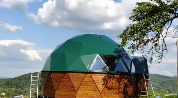 Zielony dom kopułowy z drewnianą podstawą, gotowy do zamieszkania. Sprawdź dom kopułowy pod klucz cena.