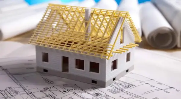 Model domu na planach architektonicznych, z widoczną konstrukcją dachu. Zastanawiasz się, ile kosztuje adaptacja projektu?