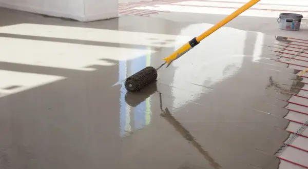 Wylewki anhydrytowe cena za 1m2. Wałek rozprowadza świeżą masę po podłodze z ogrzewaniem podłogowym.