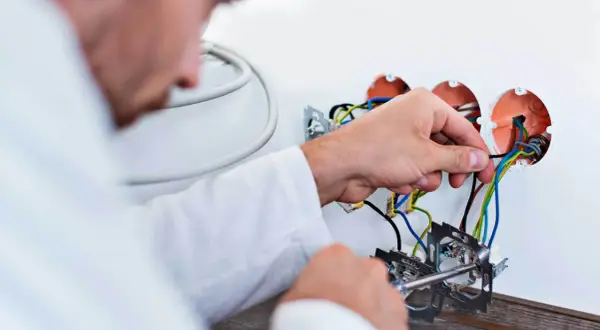 Elektryk podłącza przewody. Zastanawiasz się, ile kosztuje wymiana instalacji elektrycznej? Sprawdź!