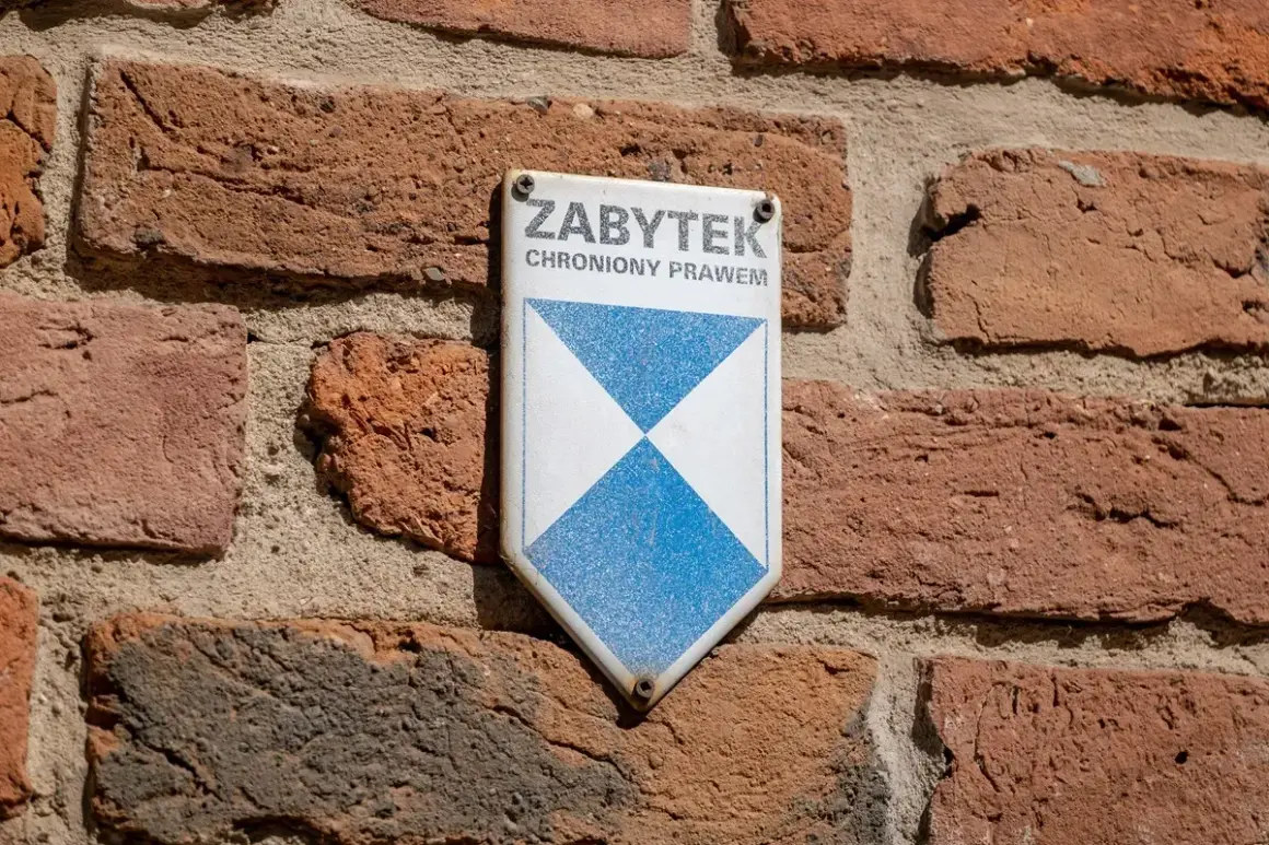 Tabliczka "ZABYTEK CHRONIONY PRAWEM" na ceglanej ścianie. To znak, że obiekt wymaga troski i konserwacji.