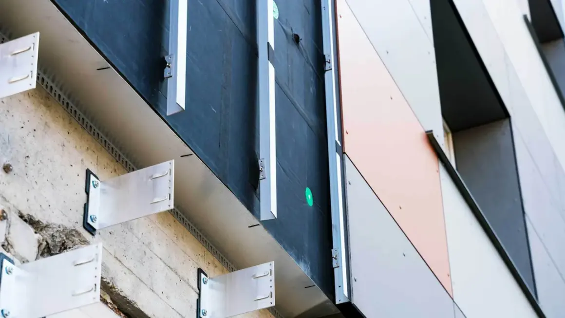 System mocowania paneli elewacyjnych, tworzący przestrzeń dla wentylowanej elewacji. Metalowe wsporniki przytwierdzone do betonu, pod czarną membraną.