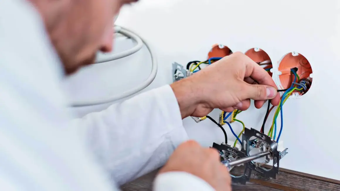 Elektryk podłącza przewody. Zastanawiasz się, ile kosztuje wymiana instalacji elektrycznej? Sprawdź!