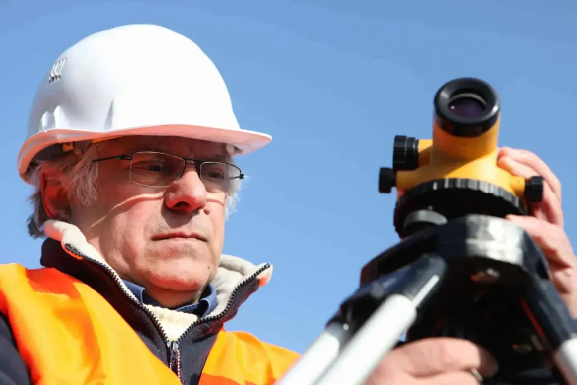 Geodeta w kasku i kamizelce odblaskowej pracuje z niwelatorem. Zastanawiasz się, ile kosztuje geodeta?
