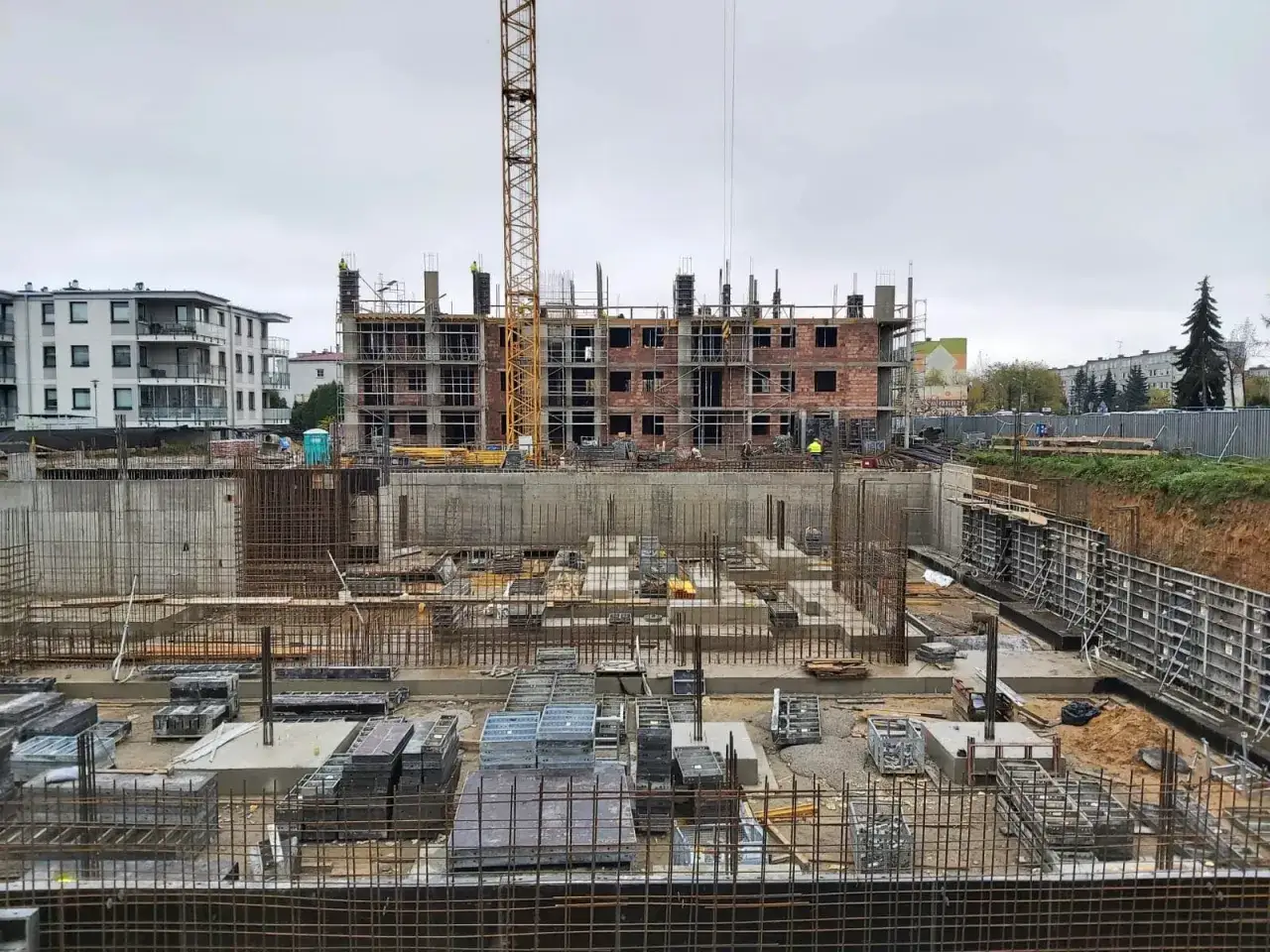 Budowa bloku mieszkalnego przez deweloperkę. Widoczny dźwig, zbrojenia, betonowe fundamenty i ściany.