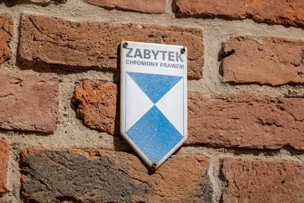 Tabliczka "ZABYTEK CHRONIONY PRAWEM" na ceglanej ścianie. To znak, że obiekt wymaga troski i konserwacji.
