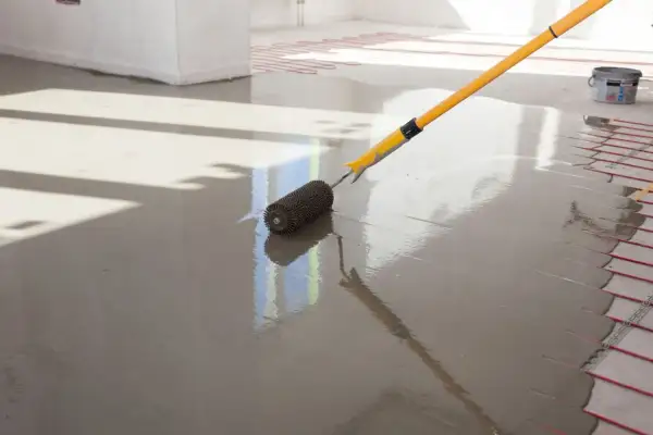 Wylewki anhydrytowe cena za 1m2. Wałek rozprowadza świeżą masę po podłodze z ogrzewaniem podłogowym.