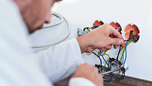 Elektryk podłącza przewody. Zastanawiasz się, ile kosztuje wymiana instalacji elektrycznej? Sprawdź!