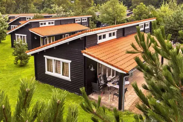 Czarny bungalow z pomarańczowym dachem, otoczony zielenią. Idealne miejsce na wakacje, zastanawiasz się bungalow co to?